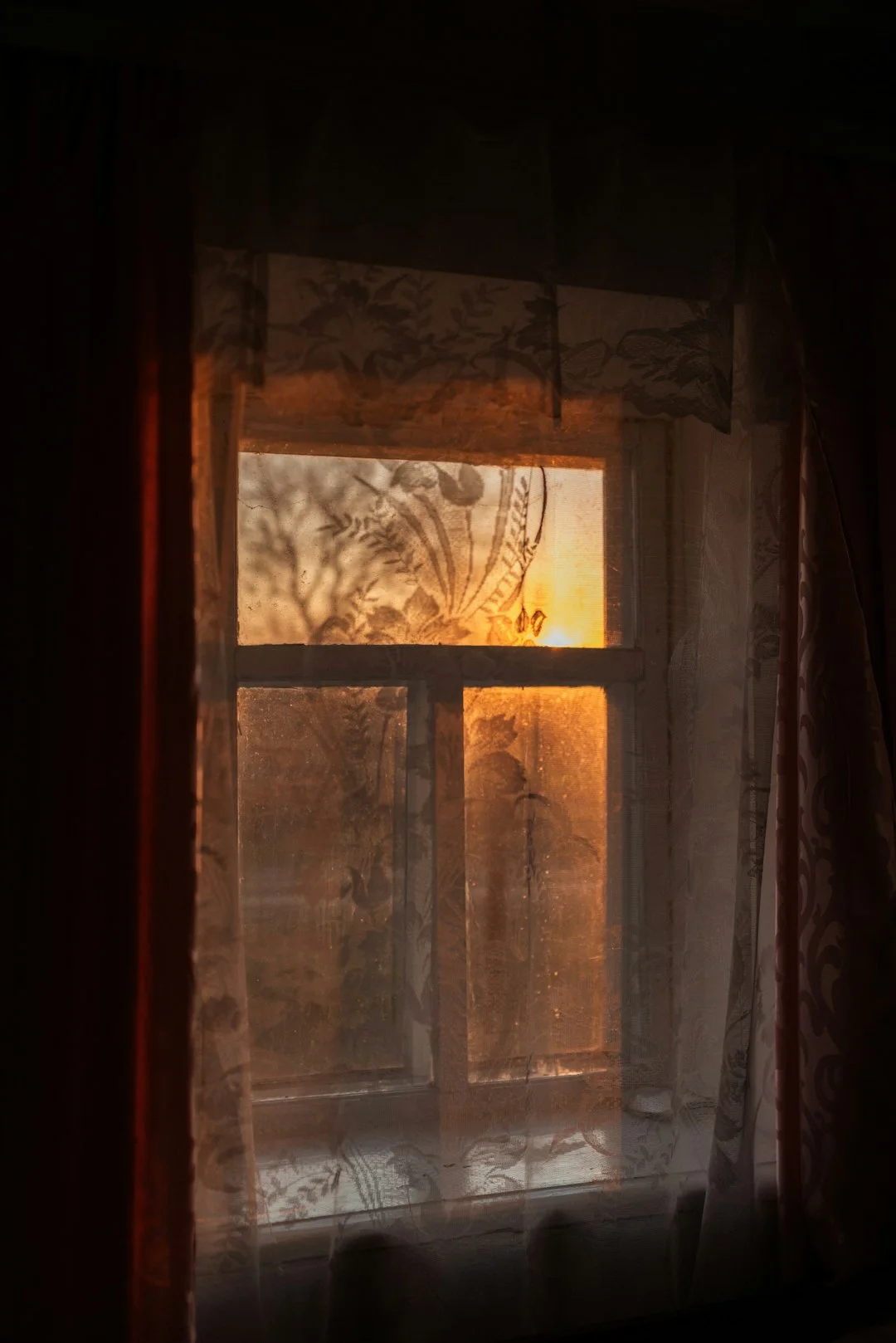 Sunset seen through a dusty window with curtains