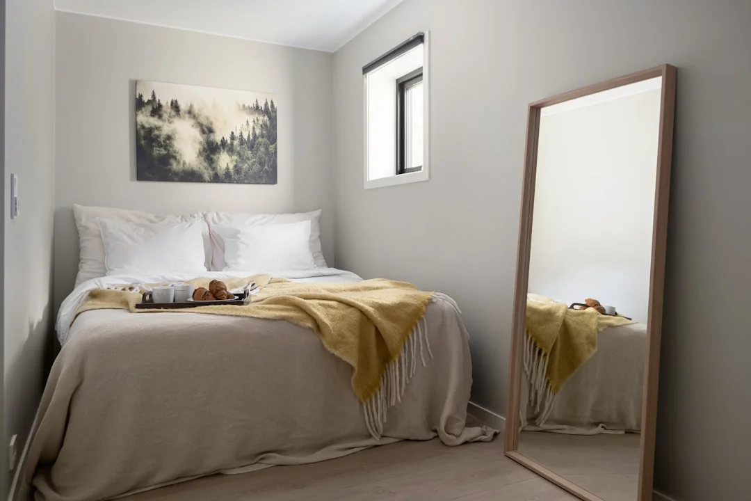 A small, cozy bedroom with a mirror that reflects the door