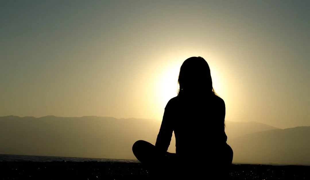A person sits in a meditative posture at sunrise in a peaceful natural setting