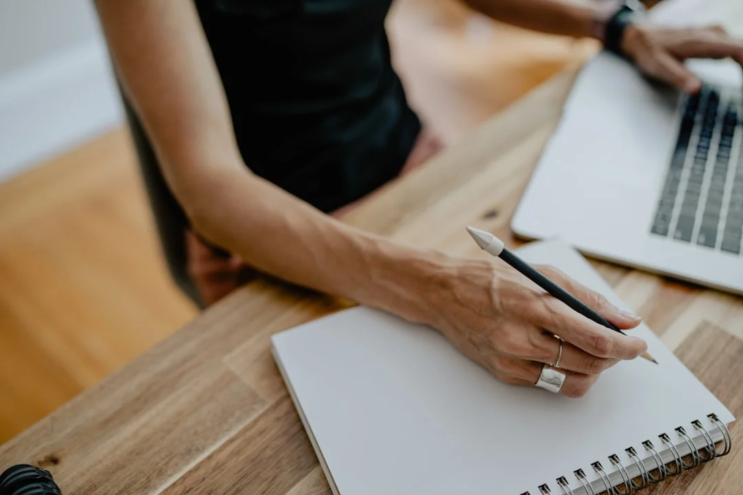 Hand scrive su un quaderno aperto posato su un tavolo di legno
