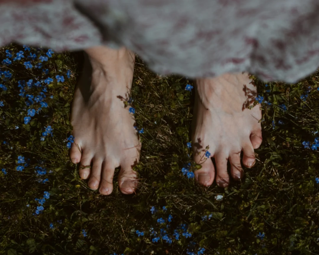A woman walks barefoot through a quiet forest, with morning light filtering through the trees