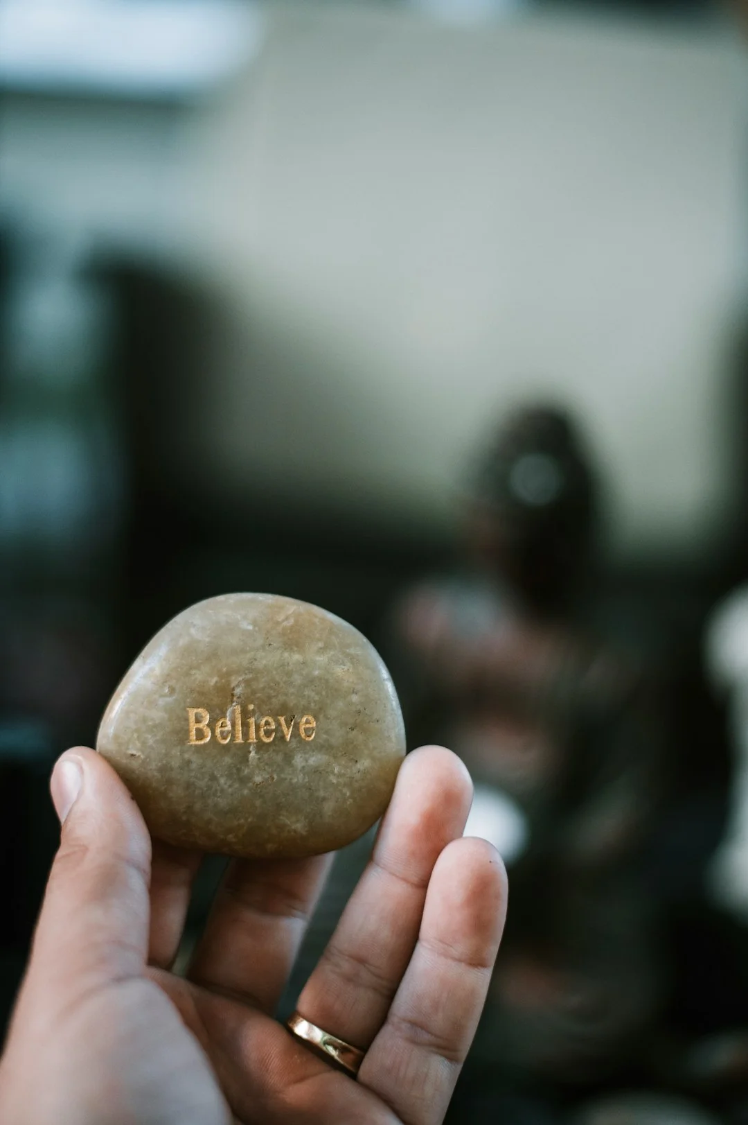 persona che tiene in mano una pietra marrone con la scritta “believe”