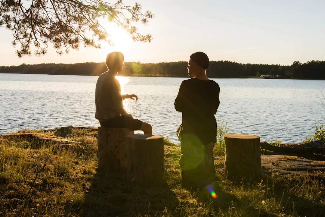 A man in a black jacket standing beside a body of water at sunset