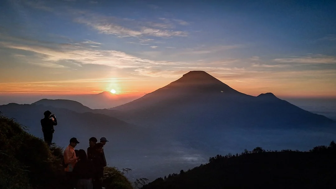 A person stands on a mountaintop at sunrise and gazes into the distance